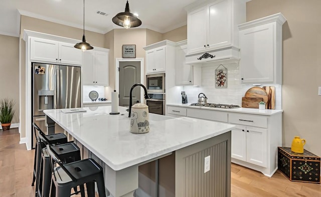 kitchen with hanging light fixtures, white cabinetry, a kitchen island with sink, and a kitchen bar