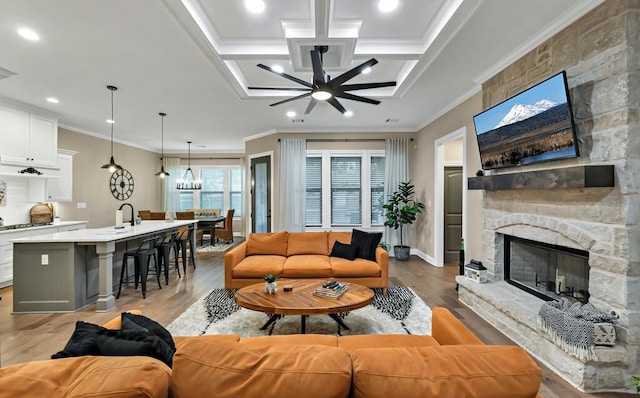 living room featuring crown molding, a stone fireplace, light hardwood / wood-style flooring, and ceiling fan