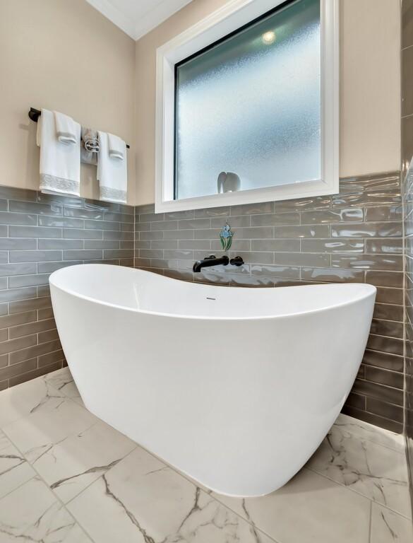 bathroom with tile walls, a bath, and ornamental molding