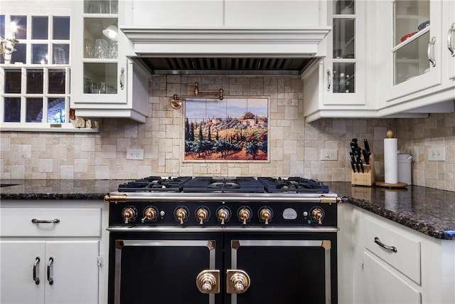 kitchen featuring backsplash, dark stone counters, high end stove, custom range hood, and white cabinetry