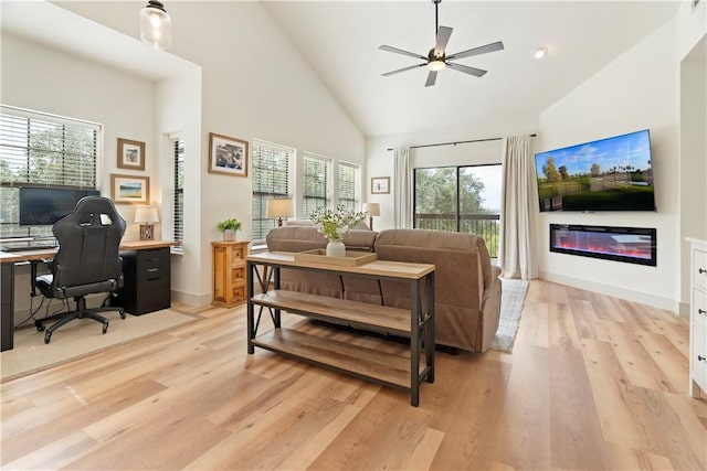 living area with ceiling fan, high vaulted ceiling, baseboards, light wood finished floors, and a glass covered fireplace