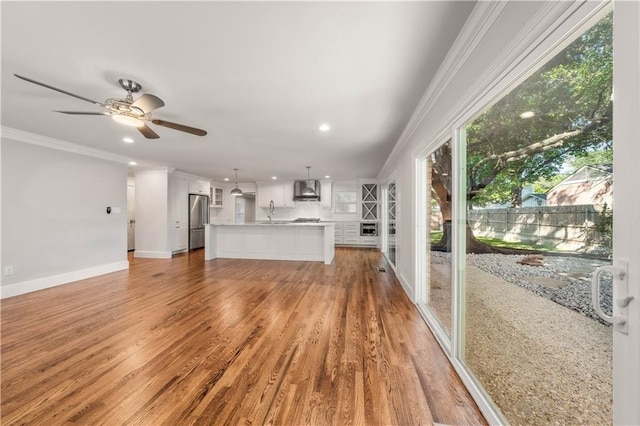 unfurnished living room featuring ceiling fan, light hardwood / wood-style flooring, sink, and ornamental molding