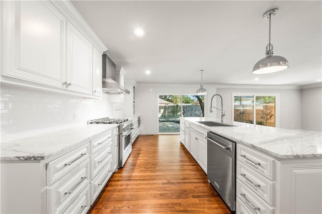 kitchen featuring sink, wall chimney exhaust hood, light wood-type flooring, appliances with stainless steel finishes, and decorative light fixtures