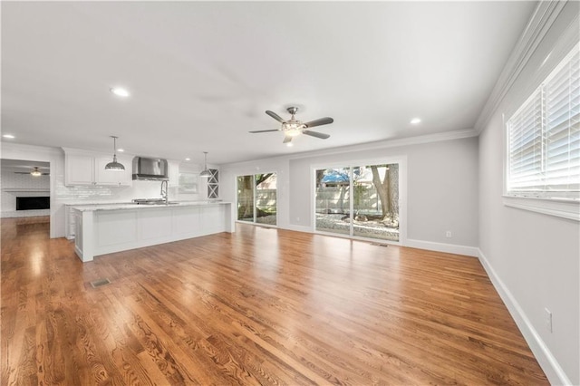 unfurnished living room with ceiling fan, a fireplace, light hardwood / wood-style floors, and ornamental molding