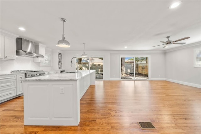 kitchen with white cabinetry, an island with sink, light hardwood / wood-style floors, and wall chimney range hood