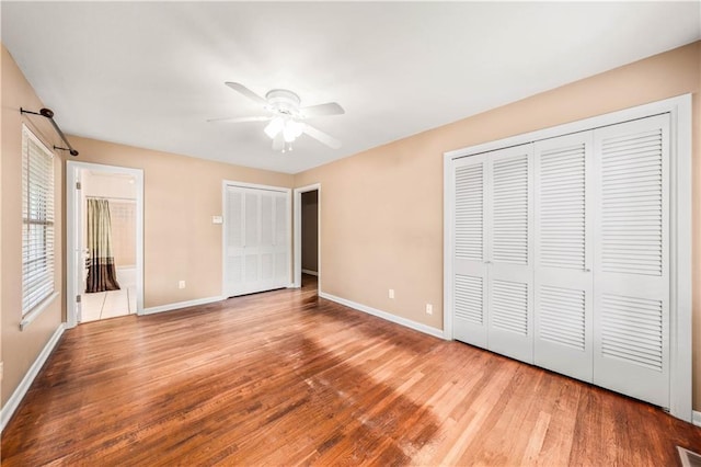 unfurnished bedroom with ceiling fan, ensuite bathroom, wood-type flooring, and two closets