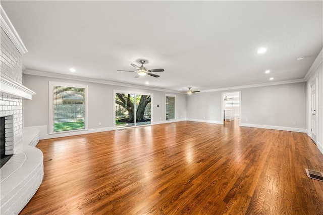 unfurnished living room featuring ceiling fan, hardwood / wood-style floors, crown molding, and a brick fireplace