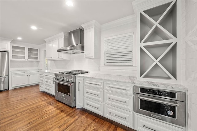 kitchen with white cabinets, wall chimney exhaust hood, stainless steel appliances, and hardwood / wood-style flooring