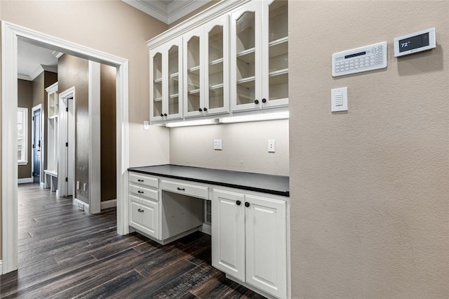 unfurnished office featuring built in desk, dark hardwood / wood-style floors, and ornamental molding