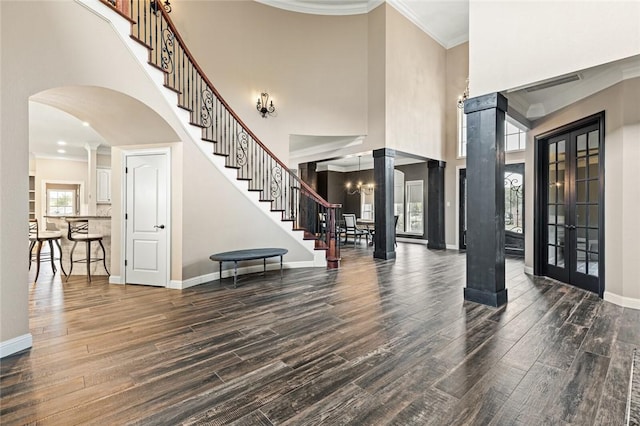 foyer with dark hardwood / wood-style floors, a towering ceiling, ornamental molding, and decorative columns