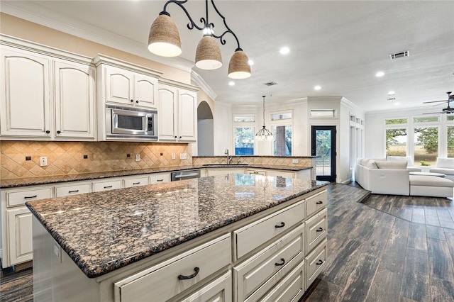 kitchen featuring dark wood-type flooring, stainless steel appliances, dark stone counters, pendant lighting, and a kitchen island