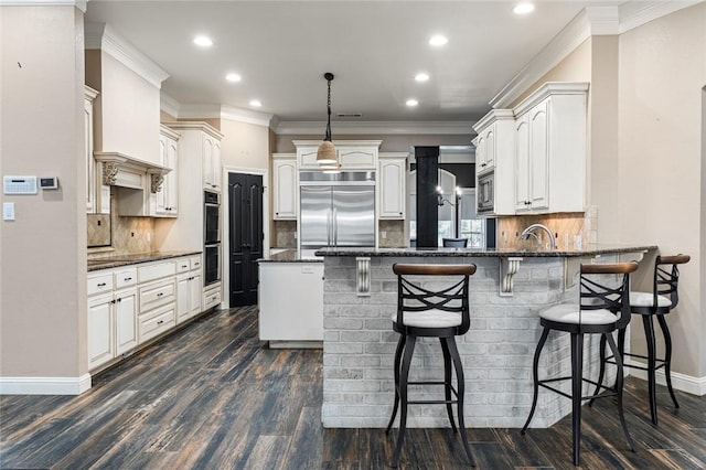 kitchen featuring hanging light fixtures, dark wood-type flooring, backsplash, built in appliances, and dark stone countertops