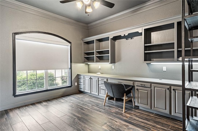 unfurnished office featuring ceiling fan, built in desk, dark hardwood / wood-style floors, and ornamental molding