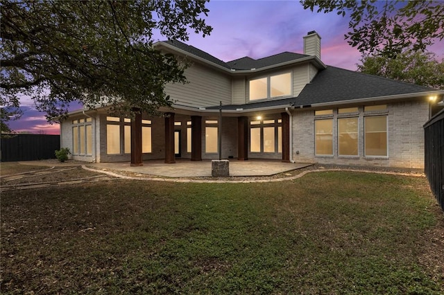 back house at dusk featuring a lawn and a patio area