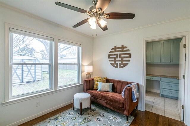 living area featuring ornamental molding, built in study area, ceiling fan, wood finished floors, and baseboards