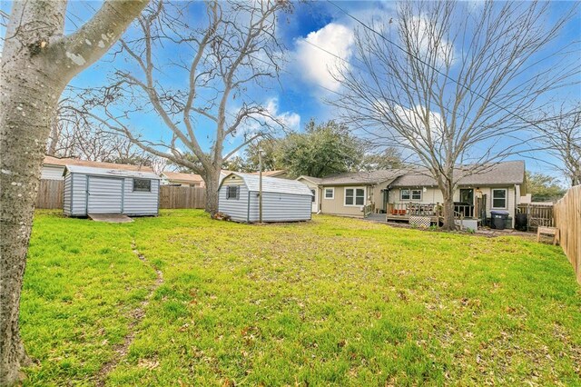 view of yard featuring a storage shed, a fenced backyard, a deck, and an outbuilding