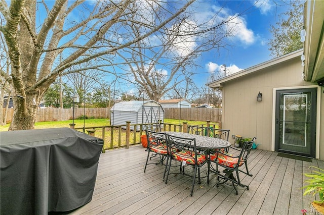 wooden deck featuring an outbuilding, outdoor dining area, a fenced backyard, grilling area, and a storage unit