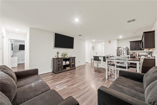 living room featuring light wood-type flooring, visible vents, baseboards, and recessed lighting