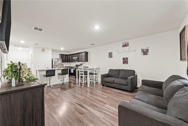 living room featuring light wood-type flooring, visible vents, and recessed lighting