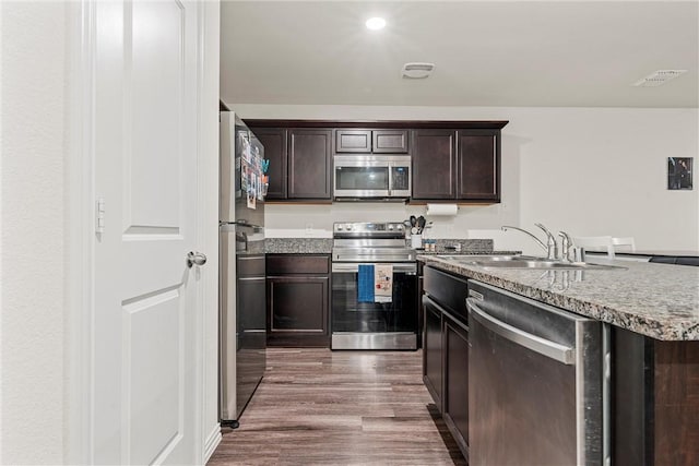 kitchen featuring visible vents, wood finished floors, light stone countertops, stainless steel appliances, and dark brown cabinets