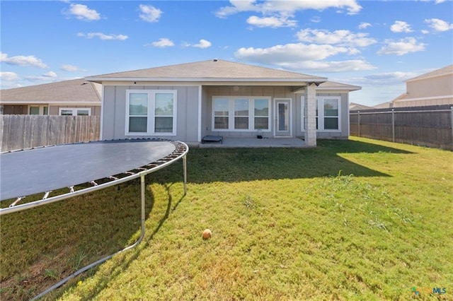 rear view of property with a patio, a yard, and a trampoline