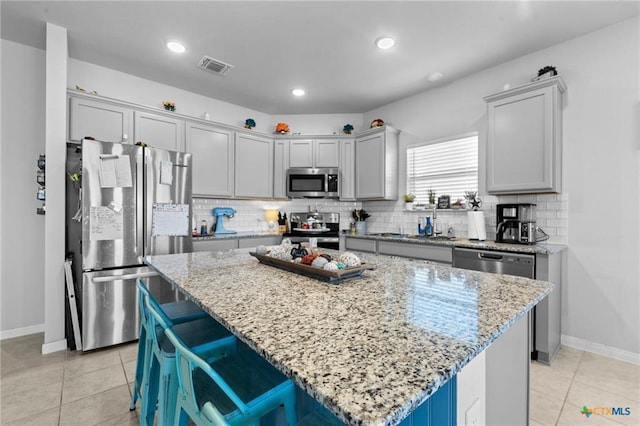 kitchen with stainless steel appliances, a center island, light tile patterned floors, and light stone countertops