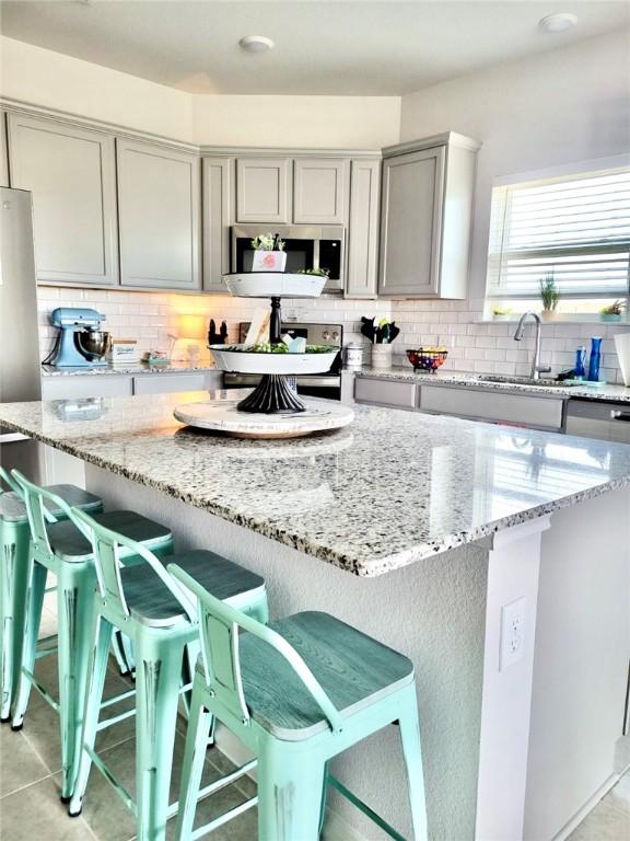 kitchen with stainless steel appliances, light stone counters, gray cabinets, and a kitchen breakfast bar