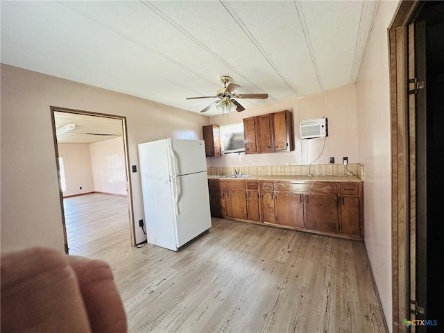 kitchen with sink, white fridge, ceiling fan, a wall unit AC, and light hardwood / wood-style flooring