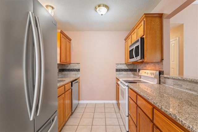 kitchen with appliances with stainless steel finishes, backsplash, light tile patterned floors, and light stone counters