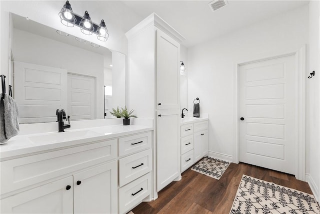 bathroom with wood finished floors, baseboards, visible vents, two vanities, and a sink