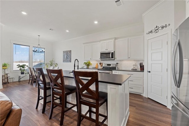 kitchen with dark wood-style flooring, stainless steel appliances, dark countertops, a notable chandelier, and backsplash