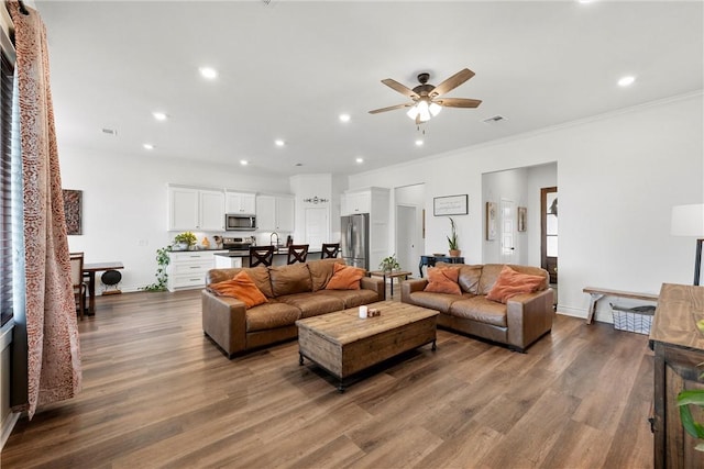 living area with a ceiling fan, dark wood-style floors, visible vents, recessed lighting, and ornamental molding