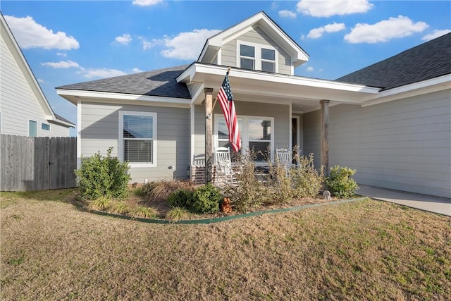 view of front of home featuring roof with shingles, covered porch, a front yard, and fence