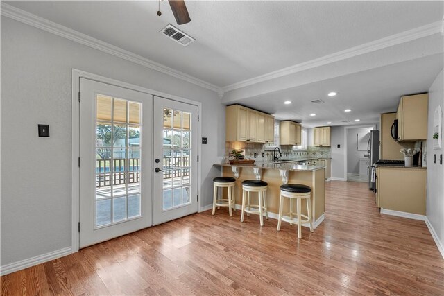 kitchen with stainless steel appliances, light stone counters, light hardwood / wood-style flooring, cream cabinets, and decorative backsplash