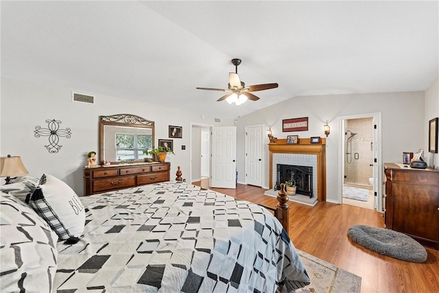 bedroom featuring a brick fireplace, vaulted ceiling, ceiling fan, connected bathroom, and light hardwood / wood-style floors