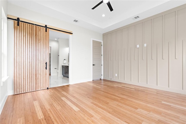 interior space with a barn door, ceiling fan, and light hardwood / wood-style floors