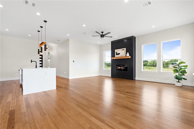 unfurnished living room with a large fireplace, ceiling fan, and light hardwood / wood-style flooring