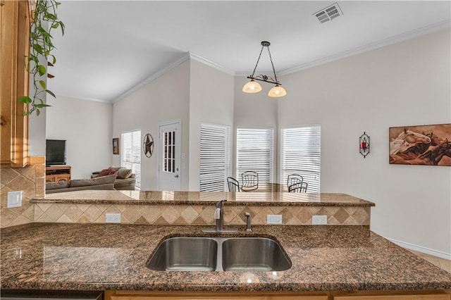 kitchen featuring sink, hanging light fixtures, dark stone countertops, decorative backsplash, and ornamental molding