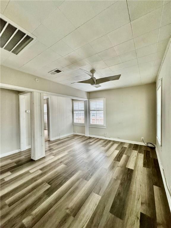 empty room with ceiling fan, wood finished floors, visible vents, and baseboards