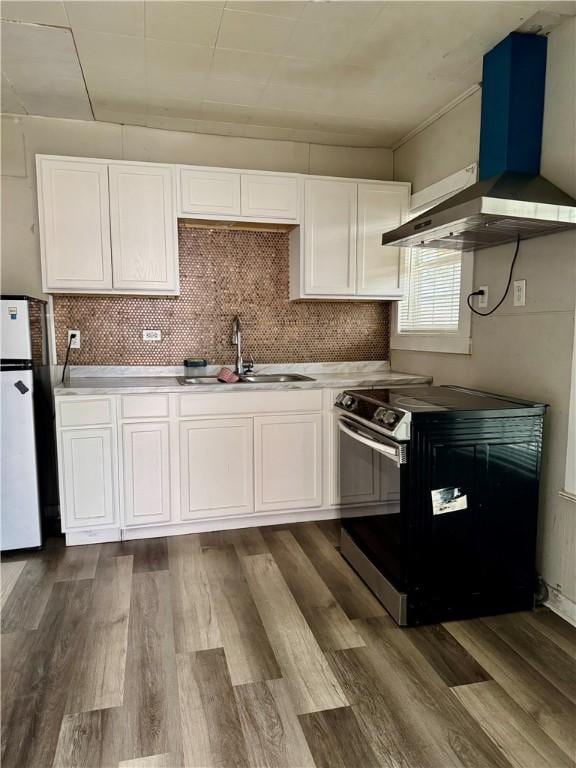 kitchen with a sink, white cabinets, wall chimney range hood, freestanding refrigerator, and electric range oven