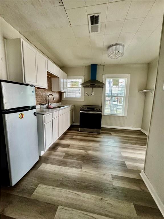 kitchen with wall chimney exhaust hood, appliances with stainless steel finishes, a sink, and white cabinetry