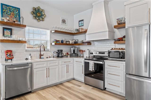 kitchen with sink, custom exhaust hood, light hardwood / wood-style flooring, stainless steel appliances, and white cabinets