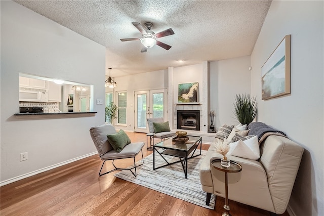 living room featuring french doors, ceiling fan with notable chandelier, hardwood / wood-style flooring, a textured ceiling, and a tiled fireplace