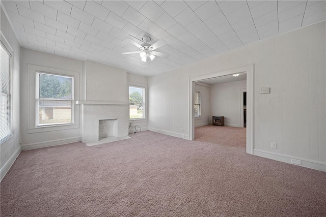 unfurnished living room featuring ceiling fan, light colored carpet, a healthy amount of sunlight, and a brick fireplace