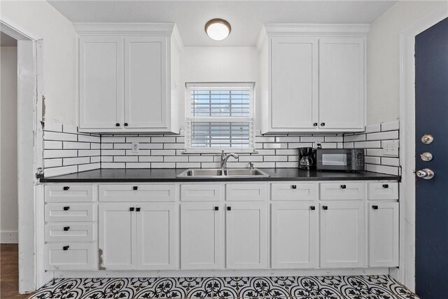 kitchen with dark countertops, white cabinets, a sink, and backsplash