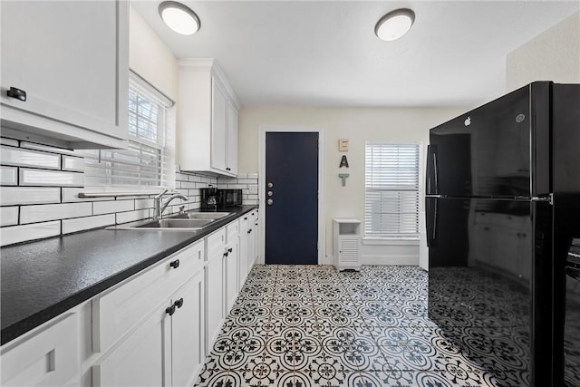 kitchen with a sink, white cabinetry, freestanding refrigerator, tasteful backsplash, and dark countertops