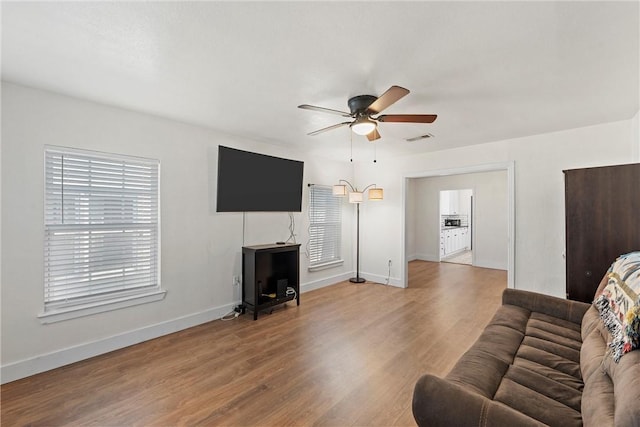 living room with a ceiling fan, visible vents, baseboards, and wood finished floors