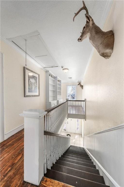 stairway with crown molding, built in shelves, and wood-type flooring