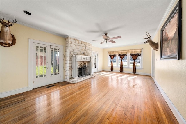 unfurnished living room with crown molding, ceiling fan, light hardwood / wood-style floors, a stone fireplace, and french doors