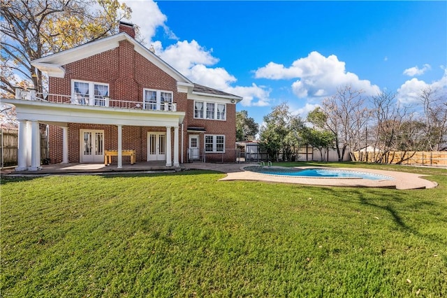 rear view of property with a fenced in pool, a lawn, a patio area, and french doors